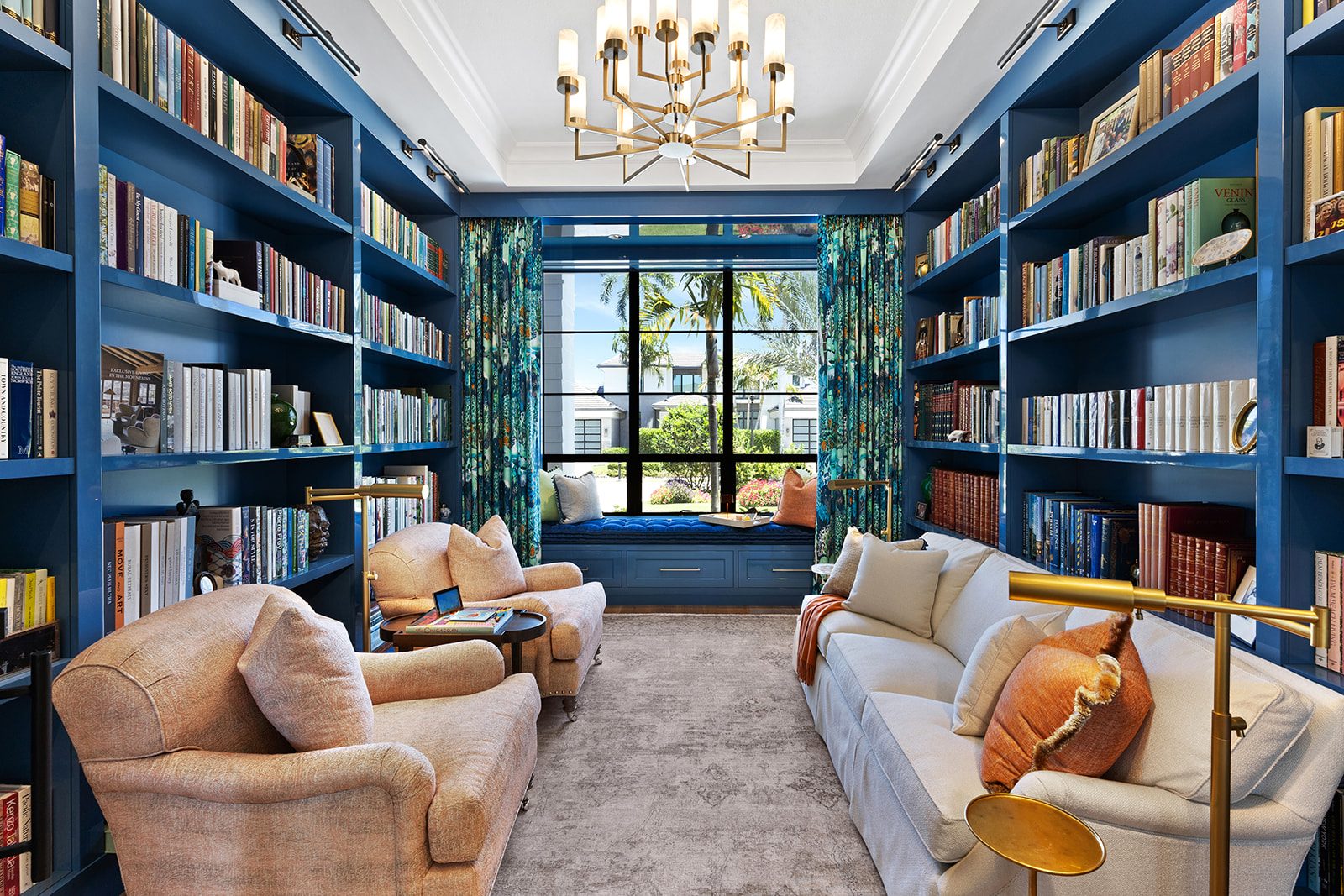 Library wrapped floor to ceiling in deep blue with a centered chandelier and window seat